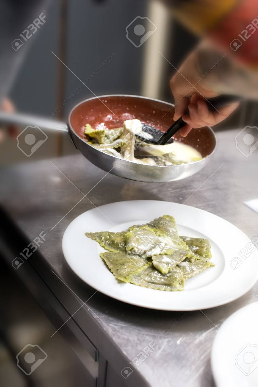 Chef plating up a serving of ravioli pasta in a restaurant kitchen spooning the noodles and