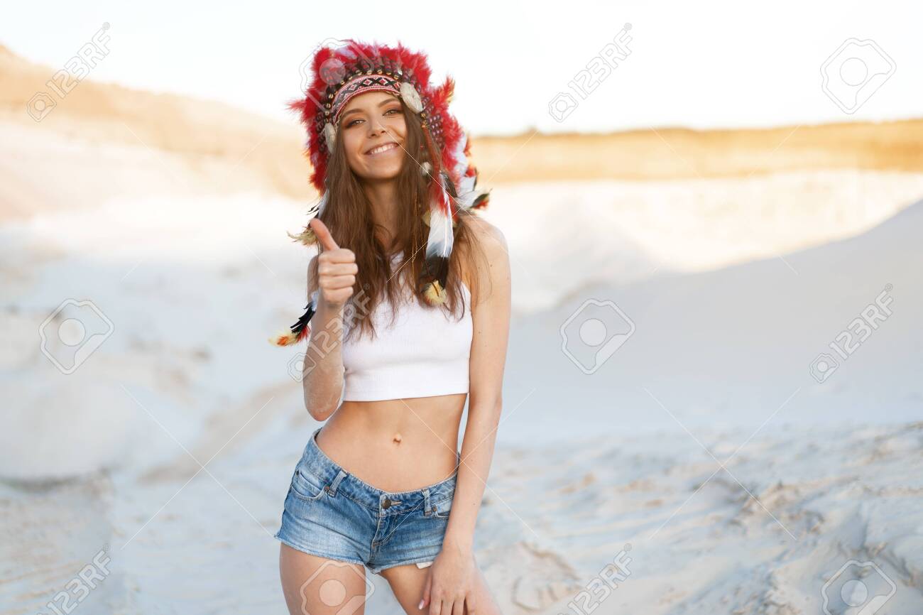 A beautiful young Caucasian girl in a white top and denim shorts. On her head wearing an Indian hat Roach. Standing in the desert. Happy holiday mood. shows thumb - 128913755 A beautiful young Caucasian girl in a white top and denim shorts. On her head wearing an Indian hat Roach. Standing in the desert. Happy holiday mood. shows thumb - 128913755