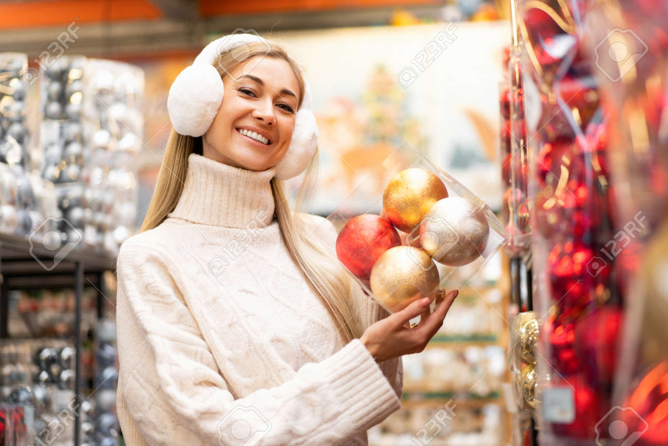 Compras de natal. a mulher escolhe a decoração de natal no supermercado. mulher caucasiana em fones de ouvido de pele vestidos camisola branca comprando ornamento de natal. prepare-se para o feriado de inverno. pessoa sorridente positiva - 190443632 Compras de natal. a mulher escolhe a decoração de natal no supermercado. mulher caucasiana em fones de ouvido de pele vestidos camisola branca comprando ornamento de natal. prepare-se para o feriado de inverno. pessoa sorridente positiva - 190443632
