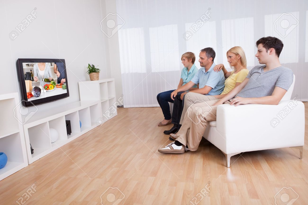 ワイド スクリーンのテレビを見ているリビング ルームのソファーに一緒に座っている 10 代の子供と家族 の写真素材 画像素材 Image