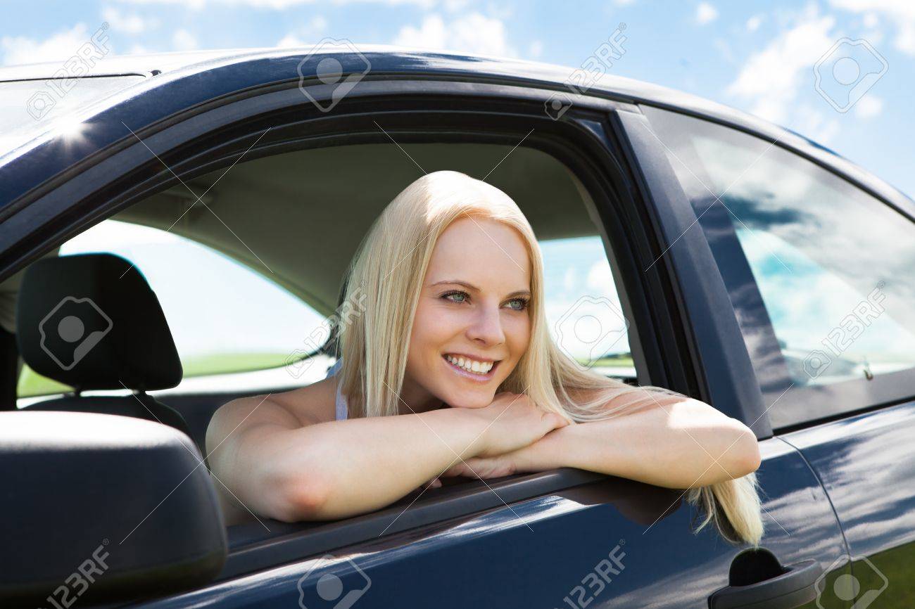 portrait of happy young blonde woman leaning on car window stock