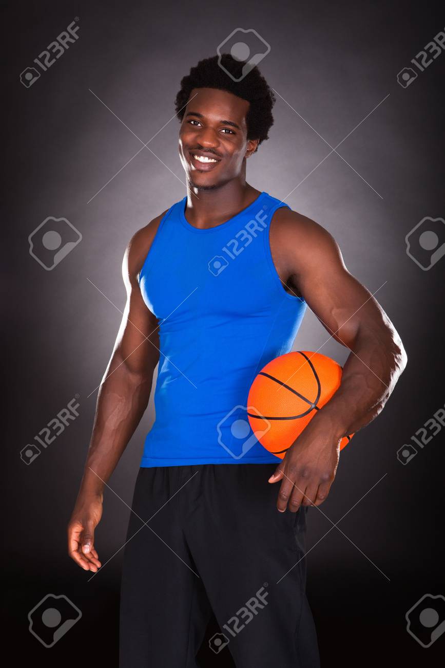 young african man holding basketball over black background stock