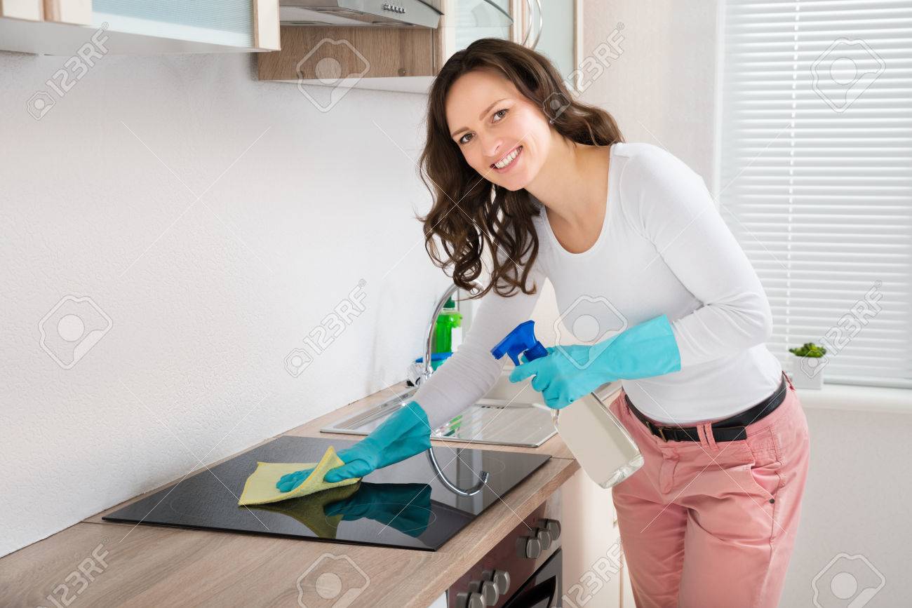 Young Woman Smiling While Cleaning Induction Hob On Countertop At Home - 43694017 Young Woman Smiling While Cleaning Induction Hob On Countertop At Home - 43694017