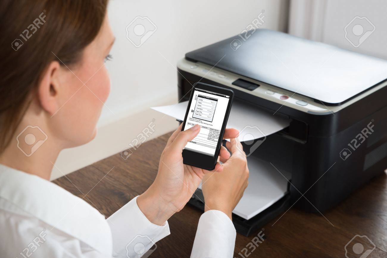 Young Businesswoman With Mobile Phone Showing Graph Connected To Printer At Desk - 45165518 Young Businesswoman With Mobile Phone Showing Graph Connected To Printer At Desk - 45165518