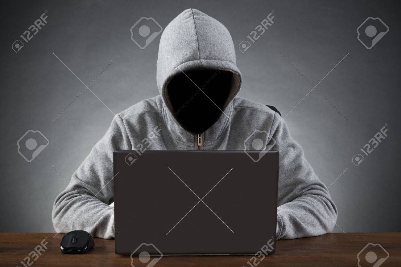 Hacker In Hood Jacket Using Laptop At Table Stock Photo Picture