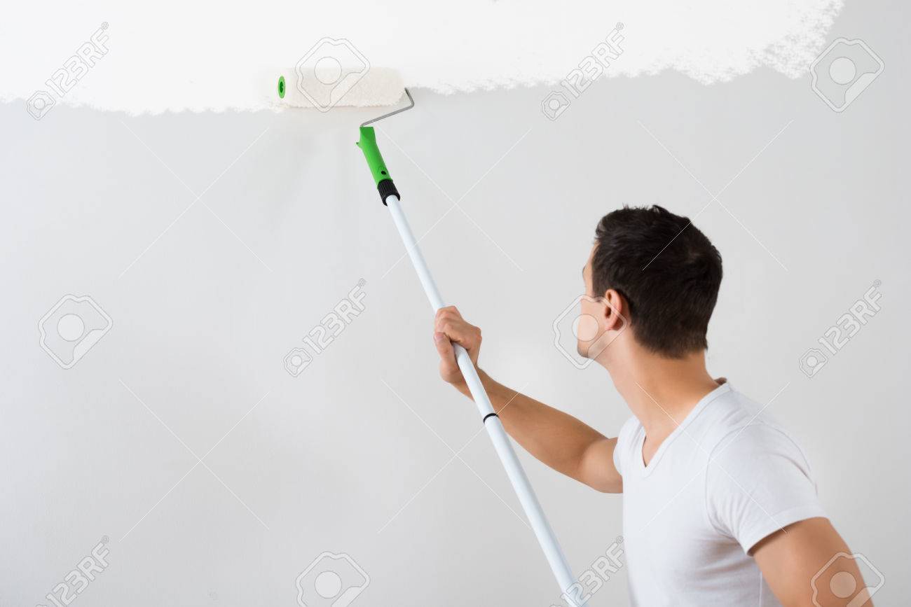 Side View Of Young Man Painting Wall With Paint Roller At Home Stock Photo Side View Of Young Man Painting Wall With Paint Roller At Home Stock Photo