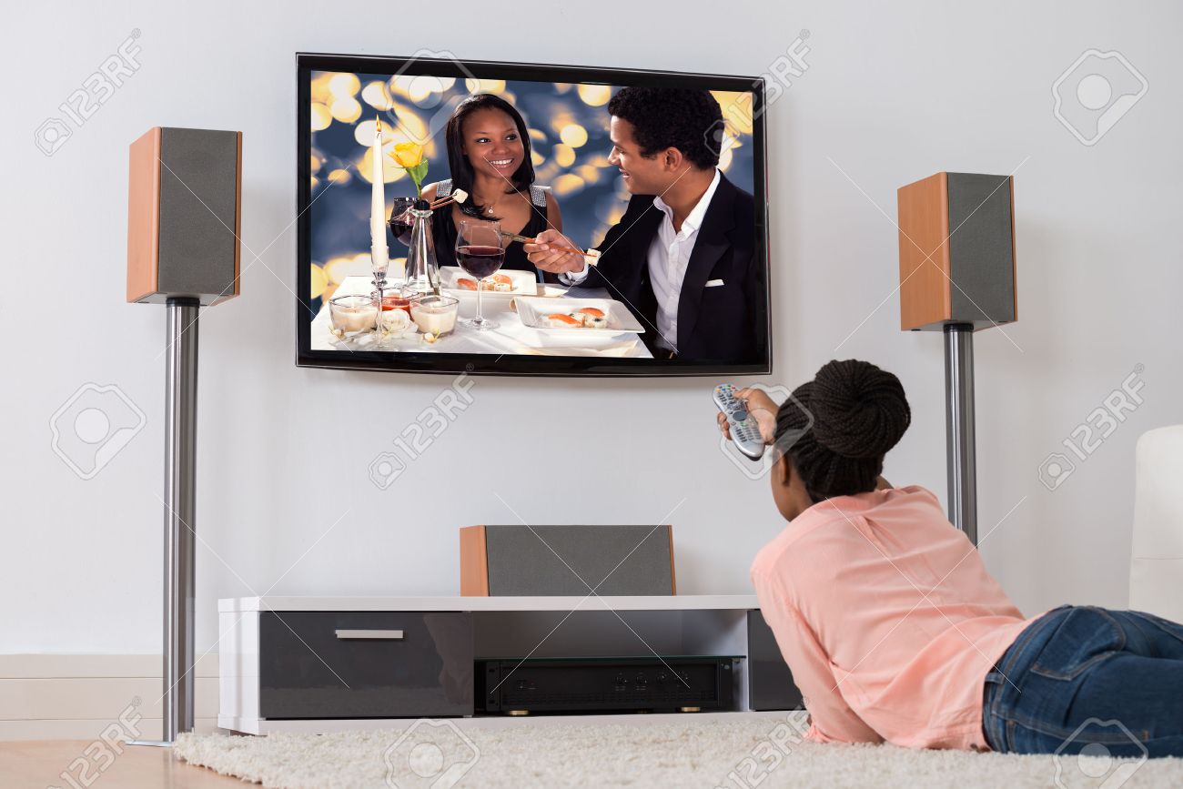 Young African Woman Lying On Carpet Watching Television - 50244321 Young African Woman Lying On Carpet Watching Television - 50244321