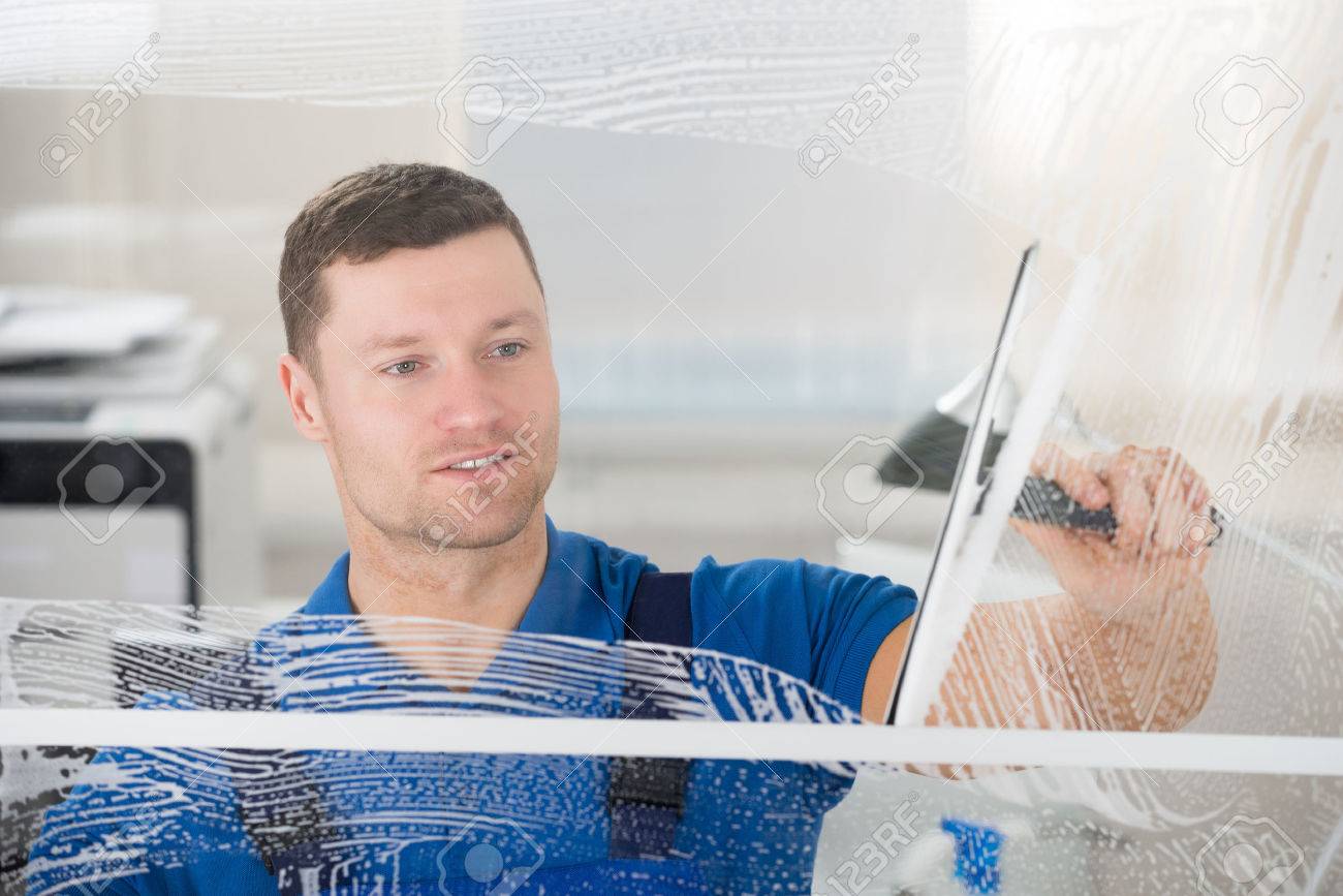 Smiling mid adult worker cleaning soap sud on glass window with squeegee - 50691542 Smiling mid adult worker cleaning soap sud on glass window with squeegee - 50691542