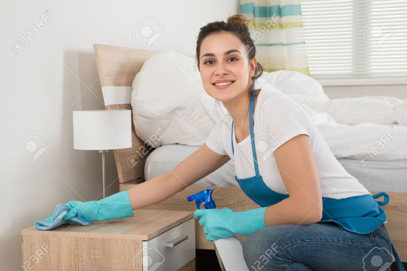 Happy Female Housekeeper Cleaning Nightstand In Room - 53332560 Happy Female Housekeeper Cleaning Nightstand In Room - 53332560