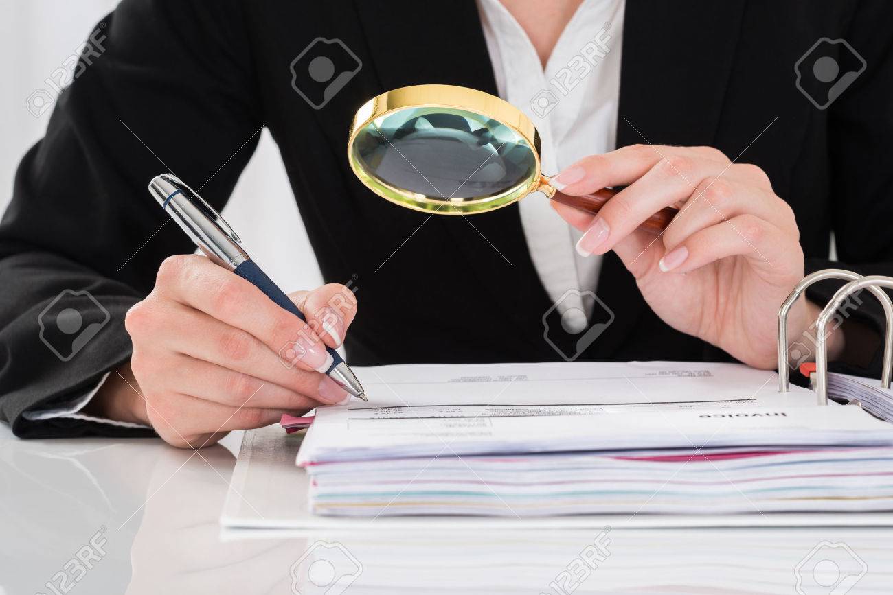 close up of auditor inspecting financial documents at desk stock