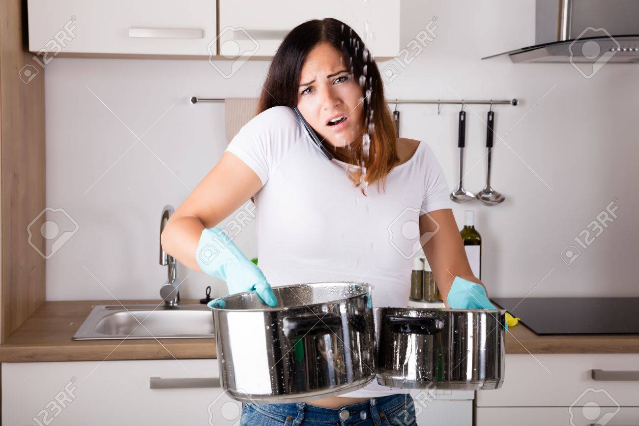 Shocked Woman Calling Plumber While Collecting Water Leaking From Ceiling Using Utensil - 69329767 Shocked Woman Calling Plumber While Collecting Water Leaking From Ceiling Using Utensil - 69329767
