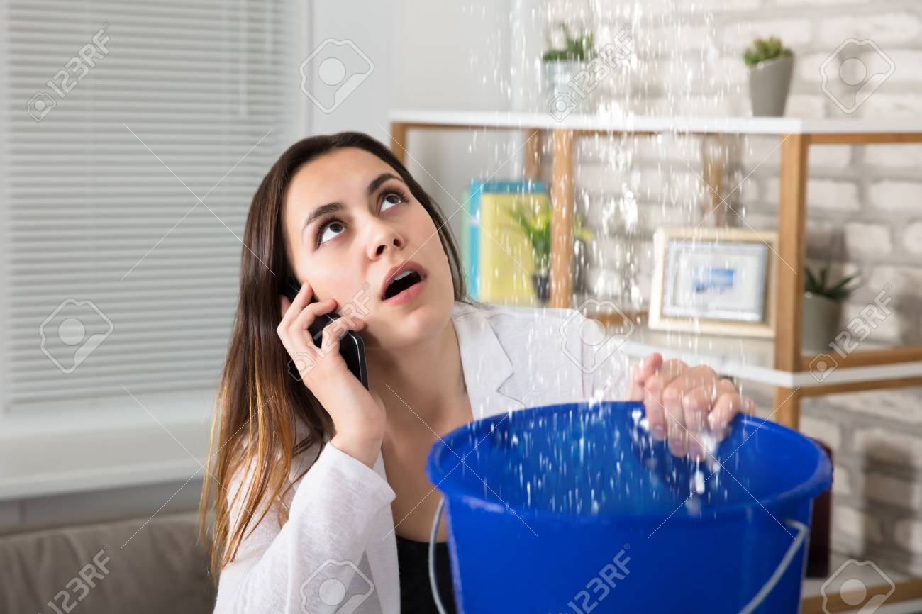Worried Woman Calling Plumber While Collecting Water Droplets Leaking From Ceiling At Home - 81652761 Worried Woman Calling Plumber While Collecting Water Droplets Leaking From Ceiling At Home - 81652761