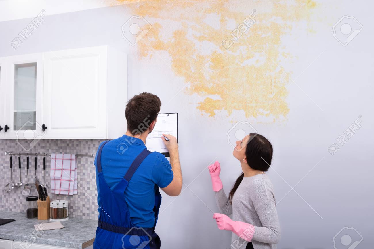 Young Worker Writing On Clipboard With Woman Standing In Kitchen - 116478153 Young Worker Writing On Clipboard With Woman Standing In Kitchen - 116478153