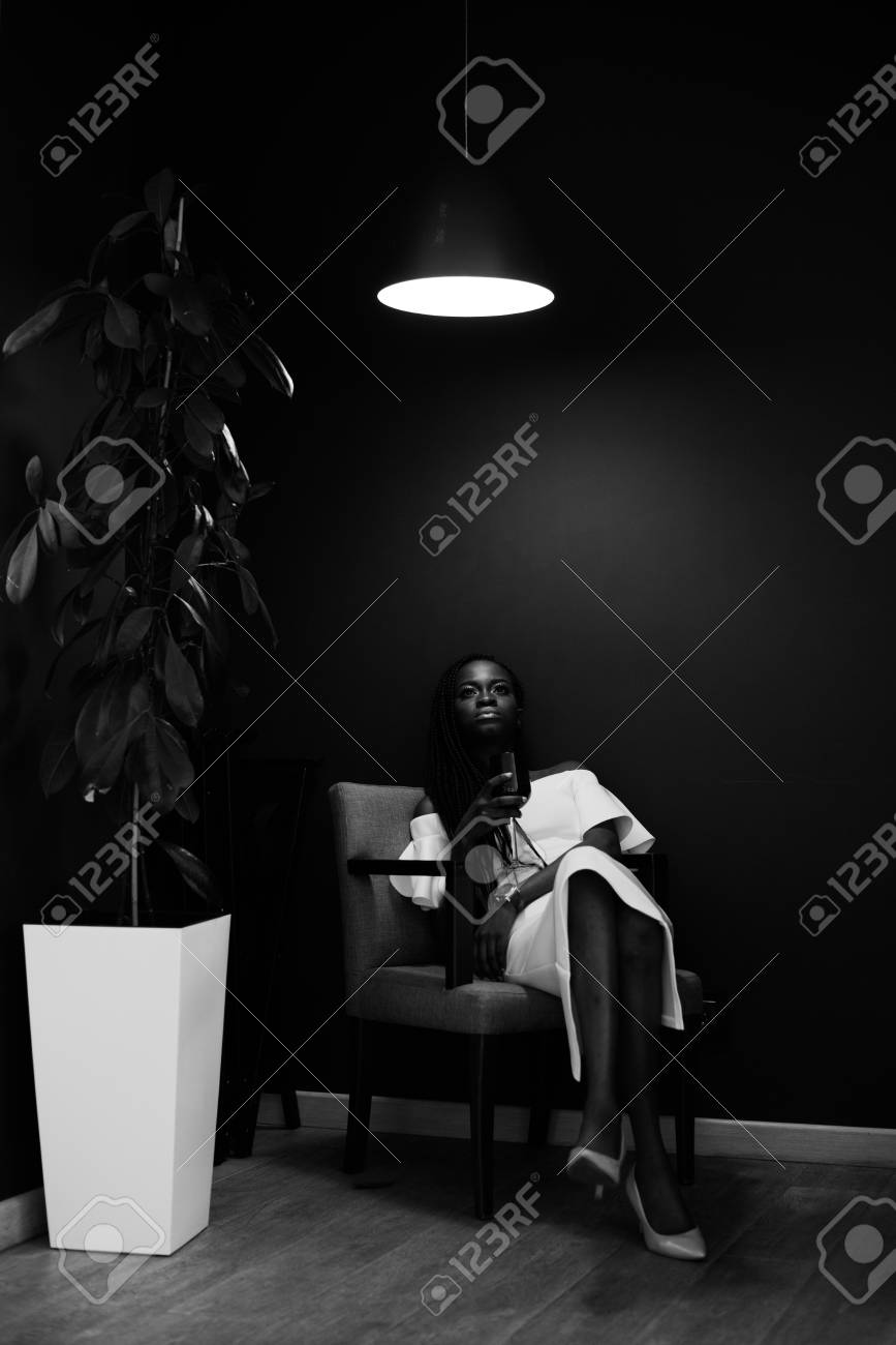 Photo Noir Et Blanc Du Modèle Africain Une Jolie Femme Est Assise Sur Le Fauteuil Près Dun Arbre Vert Dans Un Grand Pot De Fleurs Avec Un Verre