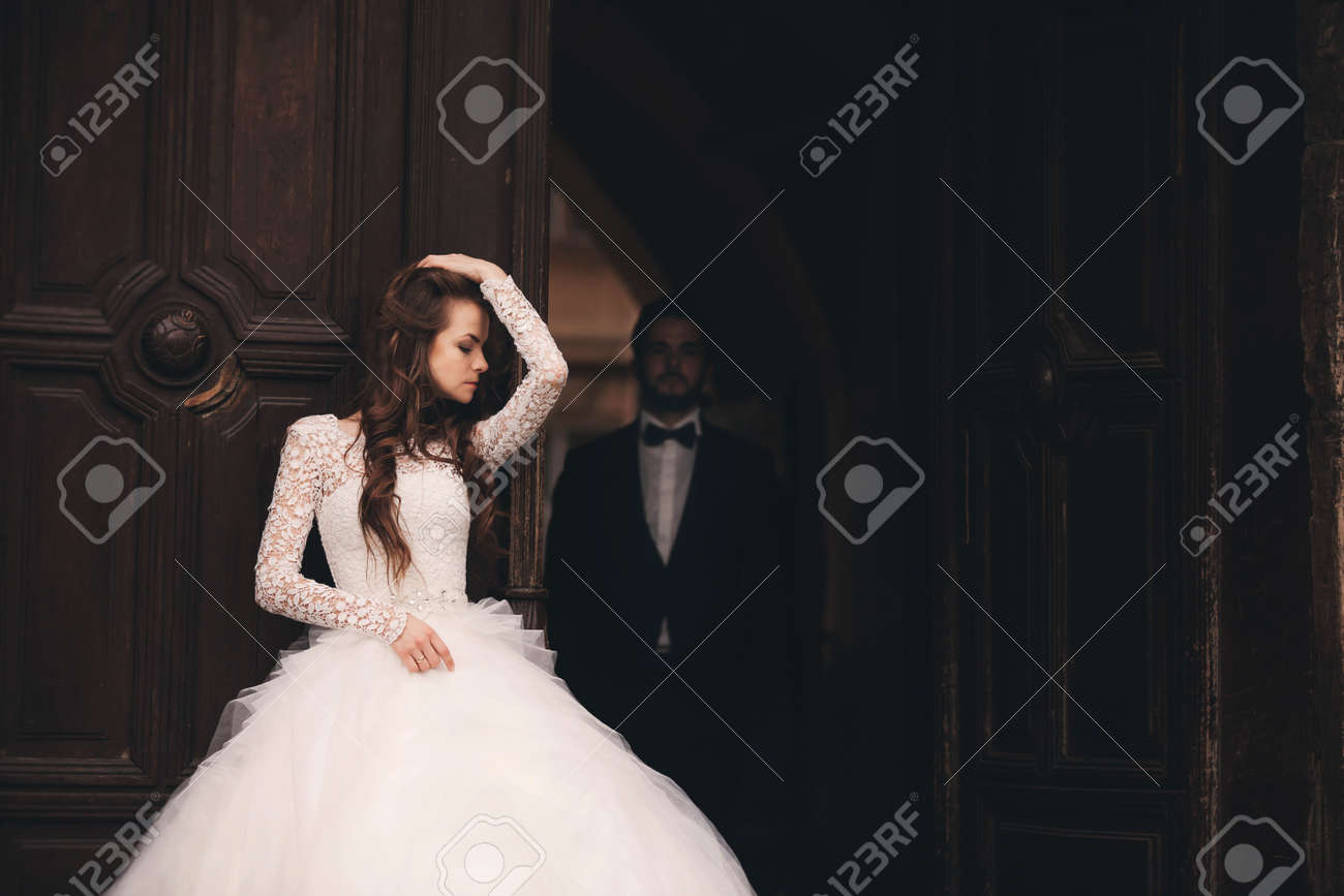 Wedding couple hugs near the vintage green door. Stone walls in ancient town background. bride with long hair in lace dress and groom in suit and bow tie. Tender embrace. Romantic love - 152951110 Wedding couple hugs near the vintage green door. Stone walls in ancient town background. bride with long hair in lace dress and groom in suit and bow tie. Tender embrace. Romantic love - 152951110