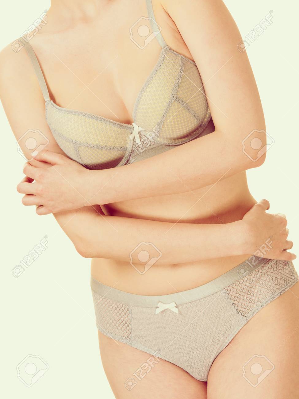 Feminidad, Ropa Interior Concepto. Mujer Delgada Atractiva Tímida En Ropa Interior Romántica Juego Con Las Manos Cruzadas Sobre El Vientre. Del Estudio Sobre Fondo Brillante Fotos, Retratos, Imágenes Y Fotografía