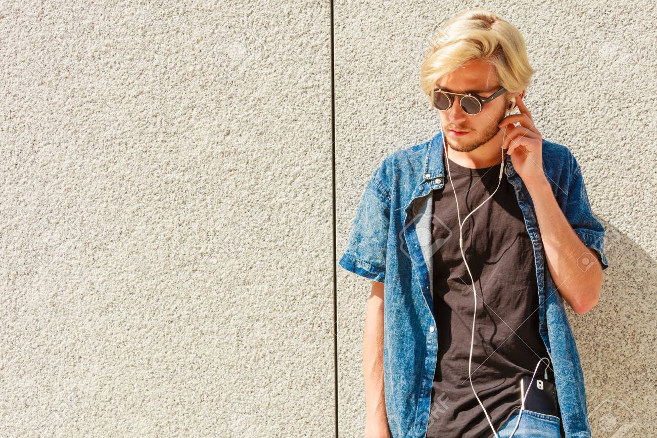 男性ファッション 技術 都会的なスタイルの服のコンセプト 流行に敏感な男市通りジーンズの服装と偏心サングラスをかけて音楽を聞くと携帯電話を保持の上に立って の写真素材 画像素材 Image