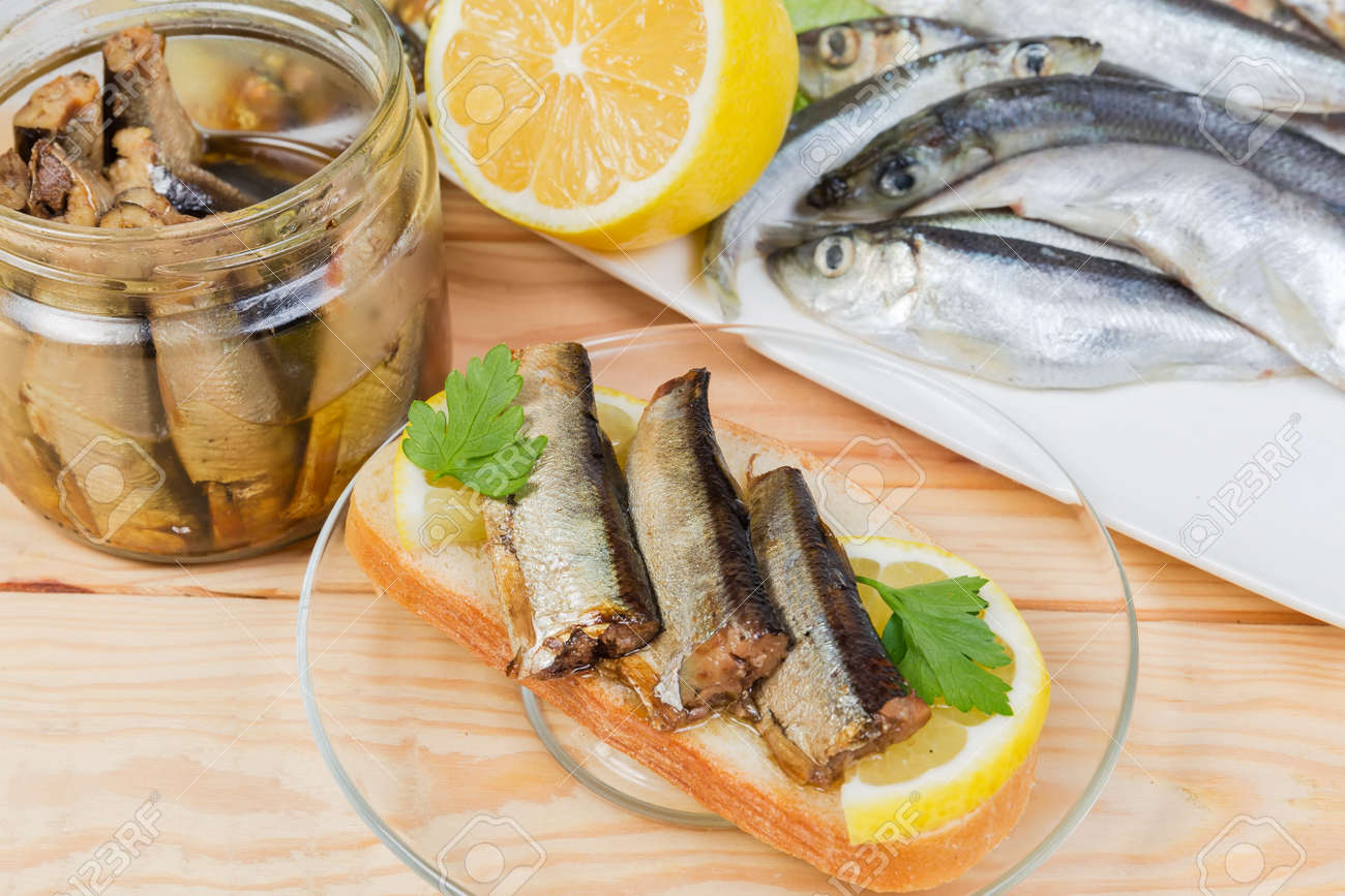 Open sandwich with smoked sprats preserved in vegetable oil and lemon slice against of some ingredients on a rustic table, close-up in selective focus - 168481273 Open sandwich with smoked sprats preserved in vegetable oil and lemon slice against of some ingredients on a rustic table, close-up in selective focus - 168481273