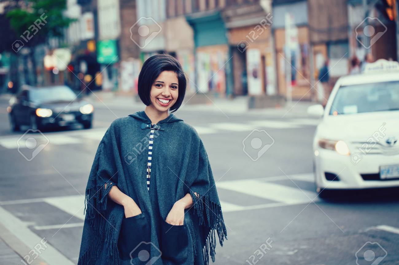 短い髪の笑顔若いヒップなラテン語ヒスパニックの女の子女性は美しいの肖像ボブ 破れたジーンズ 灰色青いポンチョ ケープ 街の外に立って の写真素材 画像素材 Image