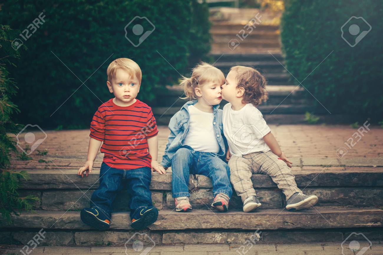 Group Of Three Cute Funny Adorable White Caucasian Children Toddlers Boys Girl Sitting Together Kissing Each Other Love Jealousy Friendship Childhood Concept Best Friends Forever Toned With Retro Filters Stock Photo Picture