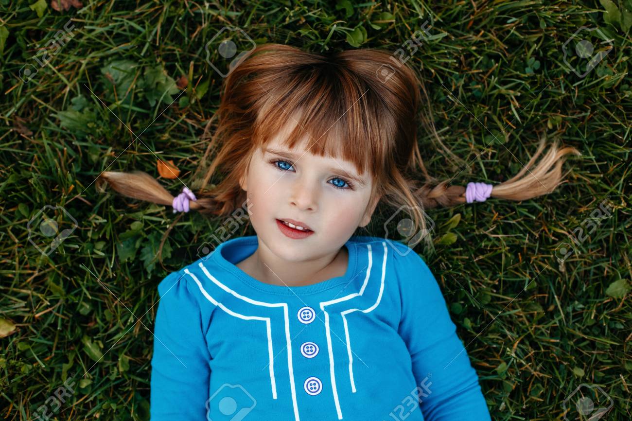 かわいい愛らしい小さな赤毛白人女の子子供のフィールド草原公園カメラの外で横になっている青いドレスのポートレート クローズ アップ 幸せな生活小児コンセプト の写真素材 画像素材 Image