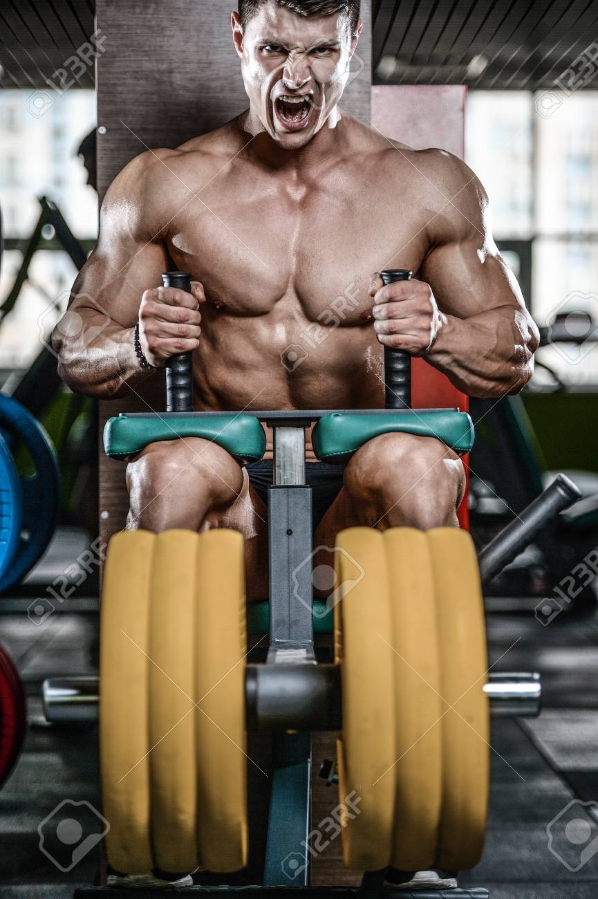 Homem Caucasiano Muscular Novo Consideravel Da Aparencia Modelo Que Da Certo No Quadriceps E Nos Isquiotibiais Dos Pes Do Treinamento Da Ginastica Em Maquinas E Com Uma Barra Que Bombeia Acima O