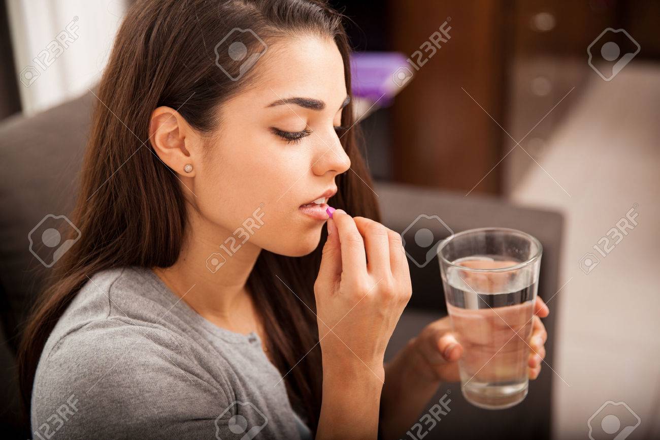 Cute young brunette taking a pill with a glass of water at home - 33909710 Cute young brunette taking a pill with a glass of water at home - 33909710