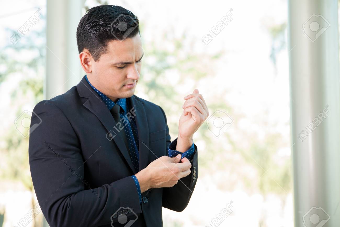 portrait of a young latin businessman fixing her suit and sleeves going on a job interview