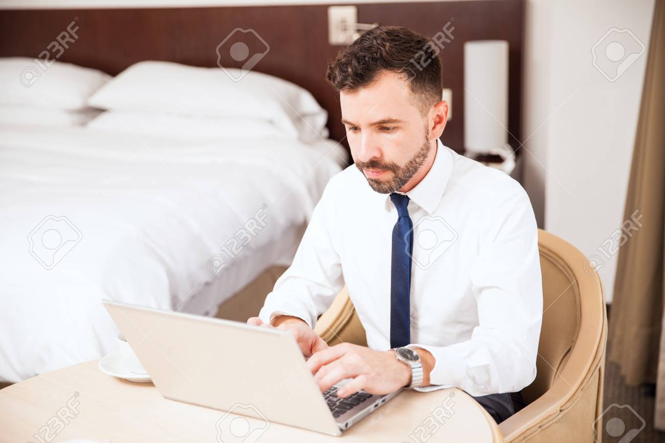 滞在ビジネス旅行中にホテルの部屋でラップトップ コンピューターに取り組んでひげ店長の若い男性 の写真素材 画像素材 Image