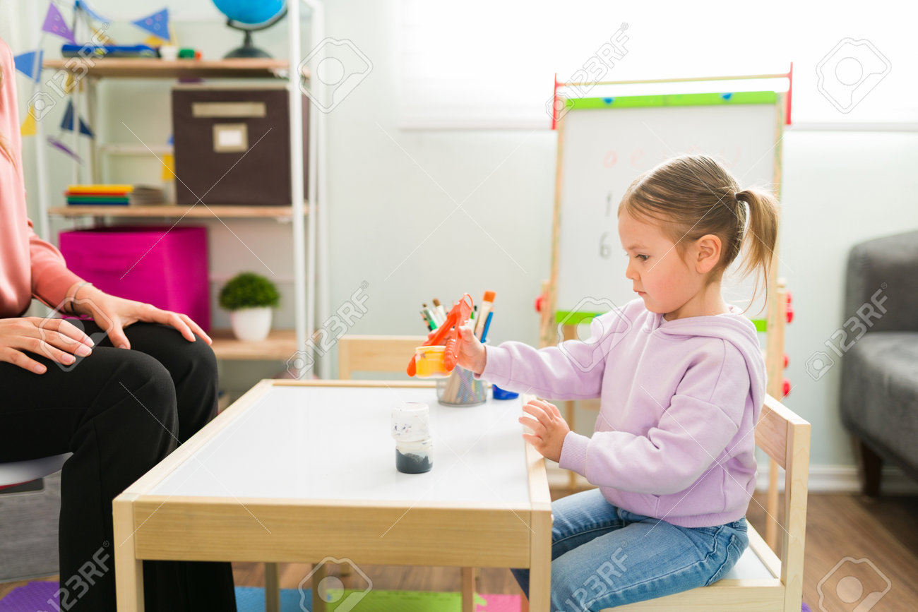 Beautiful girl holding a bottle with some tweezers during a day of homeschooling. Pretty girl learning and developing her fine motor skills - 164109296 Beautiful girl holding a bottle with some tweezers during a day of homeschooling. Pretty girl learning and developing her fine motor skills - 164109296