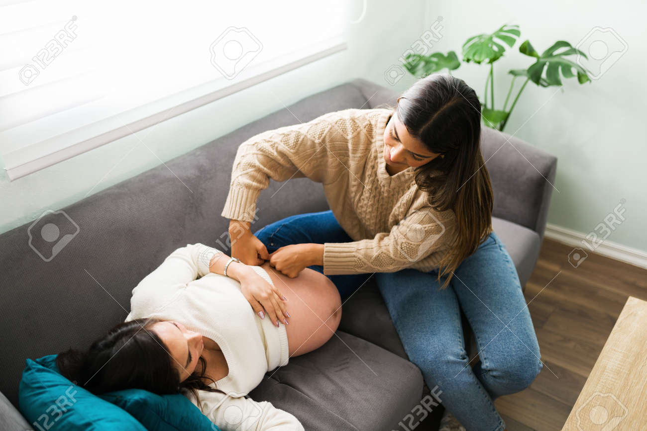 妊婦 マッサージ 画像 リビングルームで上から見た妊婦とラテンドゥーラ。ソファに横になっている妊婦の腹と腰の片側をマッサージする助産師の写真素材・画像素材 Image 164702925