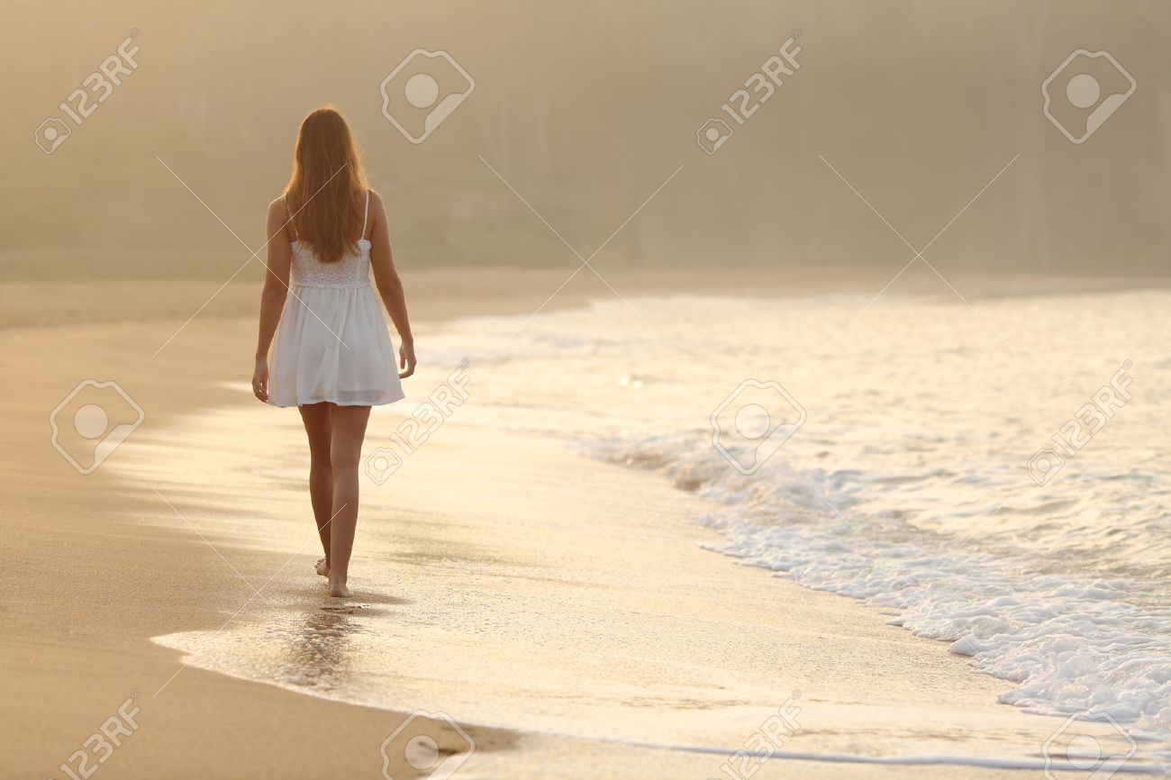 back view of a woman walking on the sand of the beach at sunset
