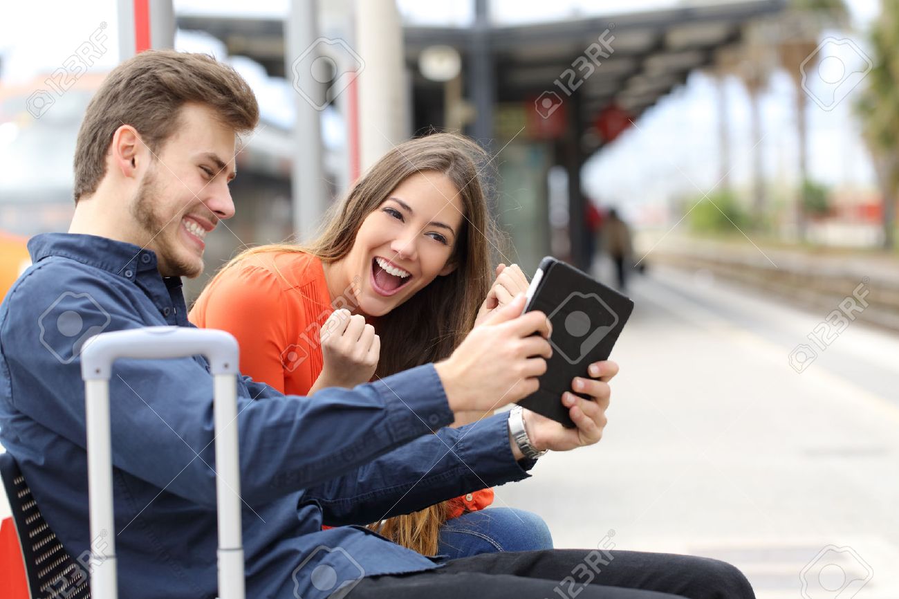 Euphoric couple watching movies or playing games in a tablet in a train station - 40441495 Euphoric couple watching movies or playing games in a tablet in a train station - 40441495