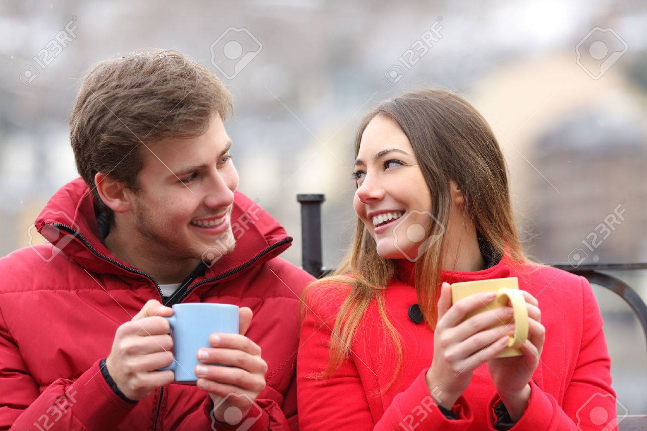 Couple talking relaxed sitting on a bench with coffee cups in winter - 50325495 Couple talking relaxed sitting on a bench with coffee cups in winter - 50325495