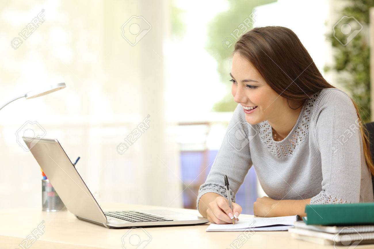 Student studying with laptop and taking notes on a desktop at home - 50532392 Student studying with laptop and taking notes on a desktop at home - 50532392