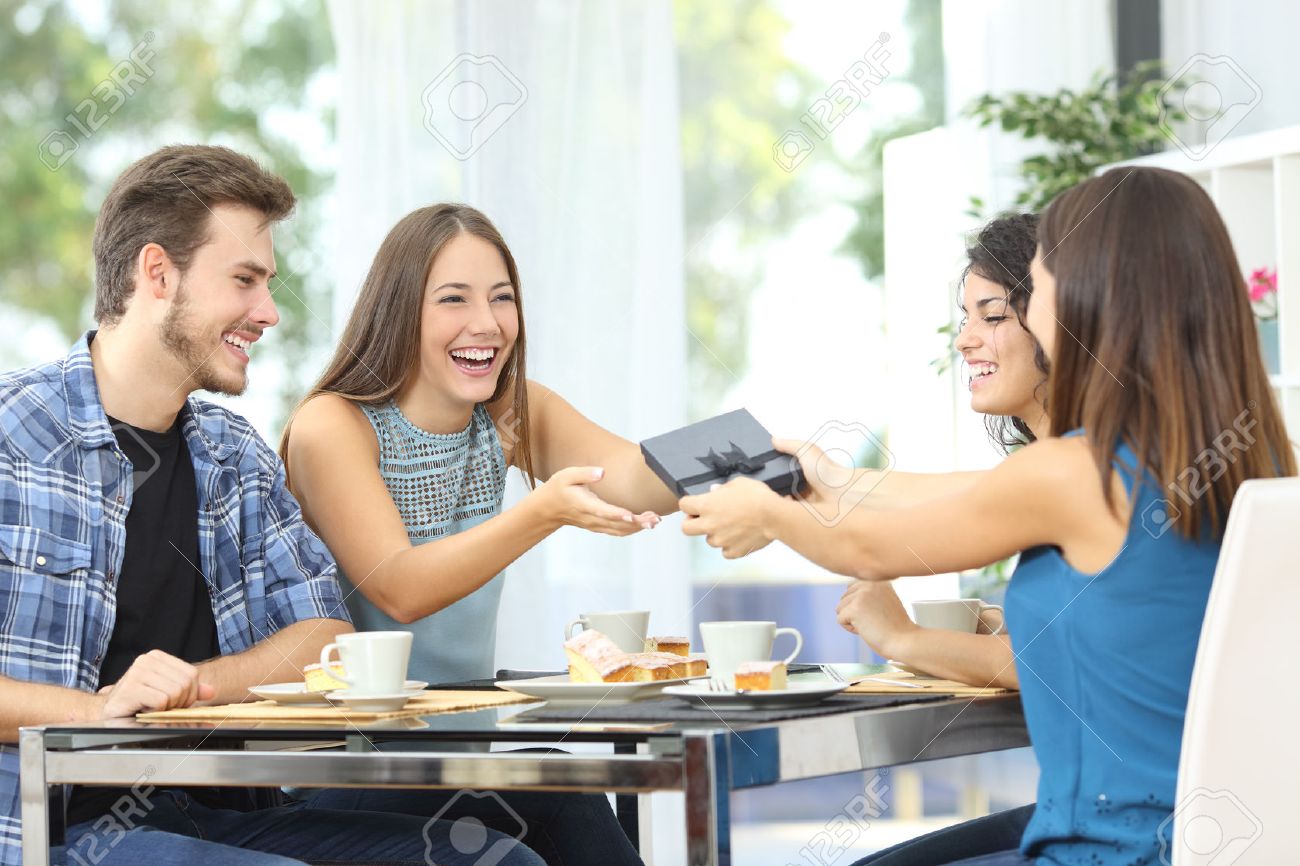 Friends celebrating birthday and giving gift to a girl sitting in a dining room - 51824889 Friends celebrating birthday and giving gift to a girl sitting in a dining room - 51824889