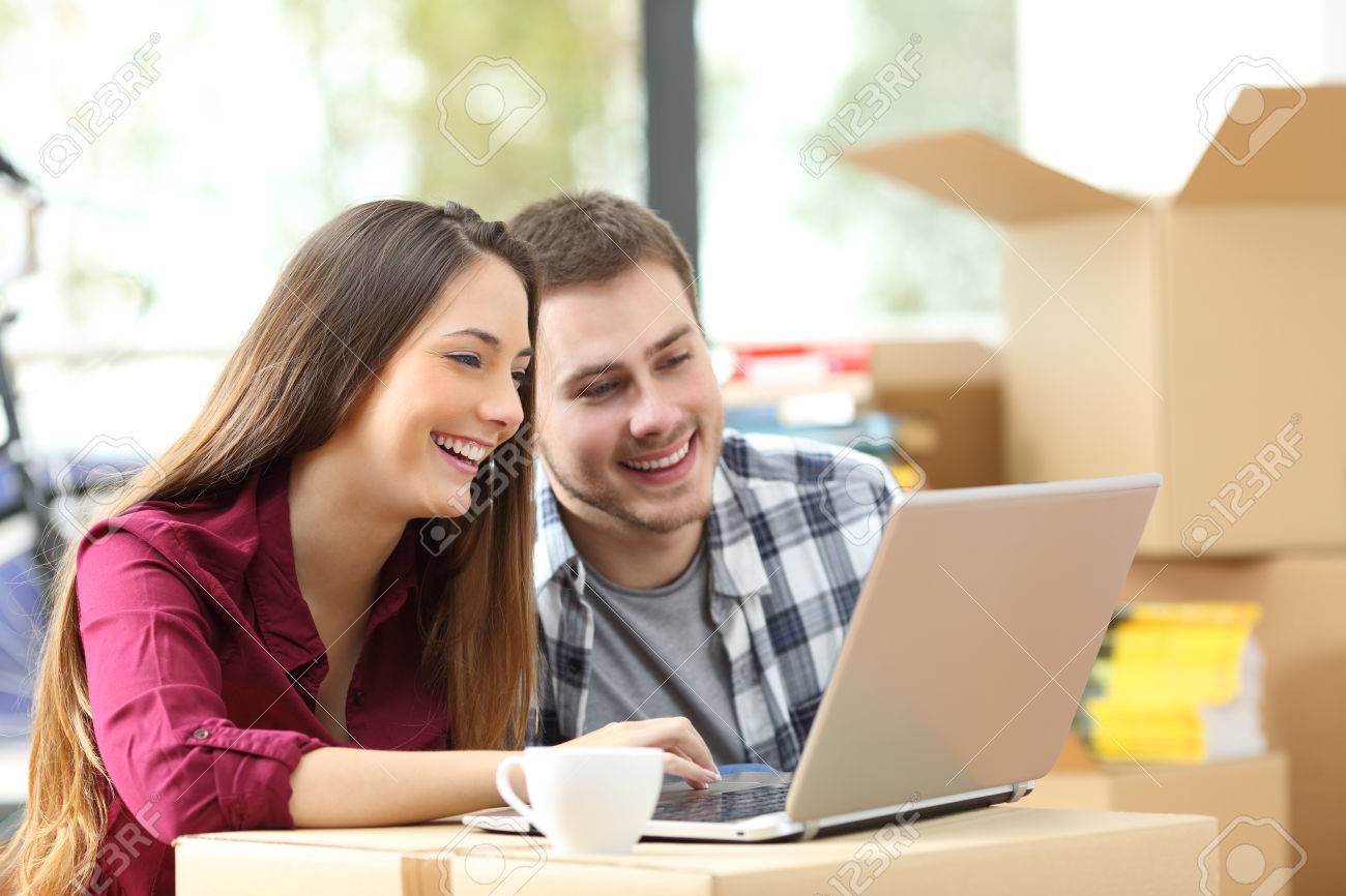 happy couple searching online with a laptop over a cardboard stock searching online