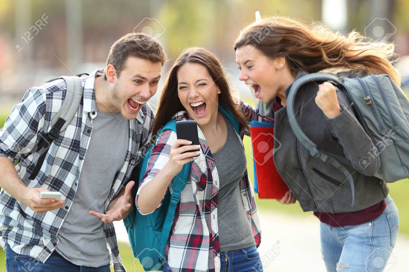 Front view of three excited students receiving good news on line in a mobile phone in an university campus or street - 82090890 Front view of three excited students receiving good news on line in a mobile phone in an university campus or street - 82090890