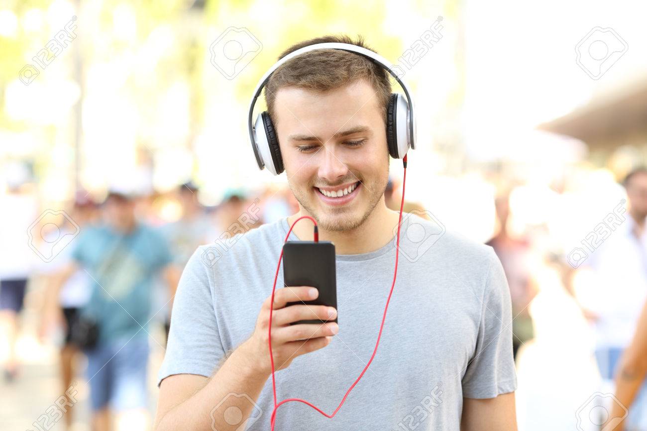 84001762-front-view-portrait-of-a-happy-boy-listening-to-music-holding-a-smart-phone-and-walking-on-the-stree.jpg