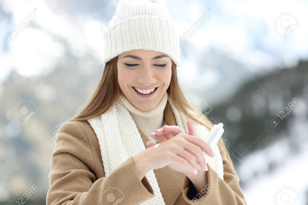 Front view portrait of a happy woman applying moisturizer cream to hydrate hands with a snowy mountain in the background - 91383648 Front view portrait of a happy woman applying moisturizer cream to hydrate hands with a snowy mountain in the background - 91383648
