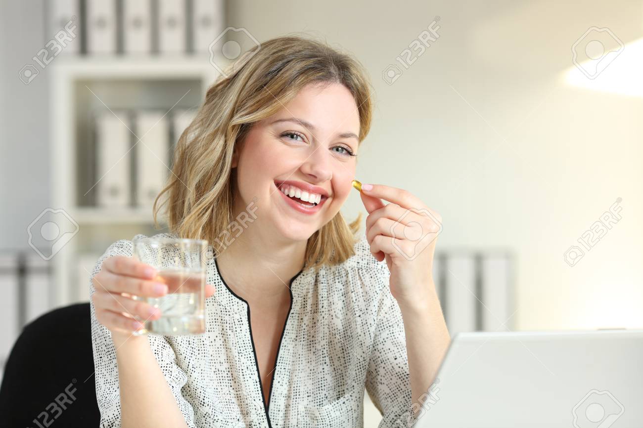 Happy office worker showing a vitamin supplement pill and a water glass looking at camera - 102077414 Happy office worker showing a vitamin supplement pill and a water glass looking at camera - 102077414
