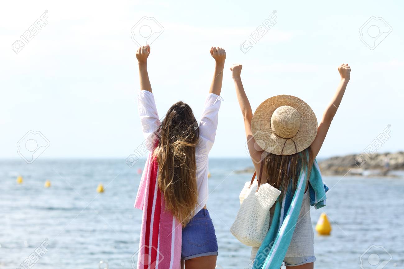 back view portrait of two excited tourists raising arms celebrating