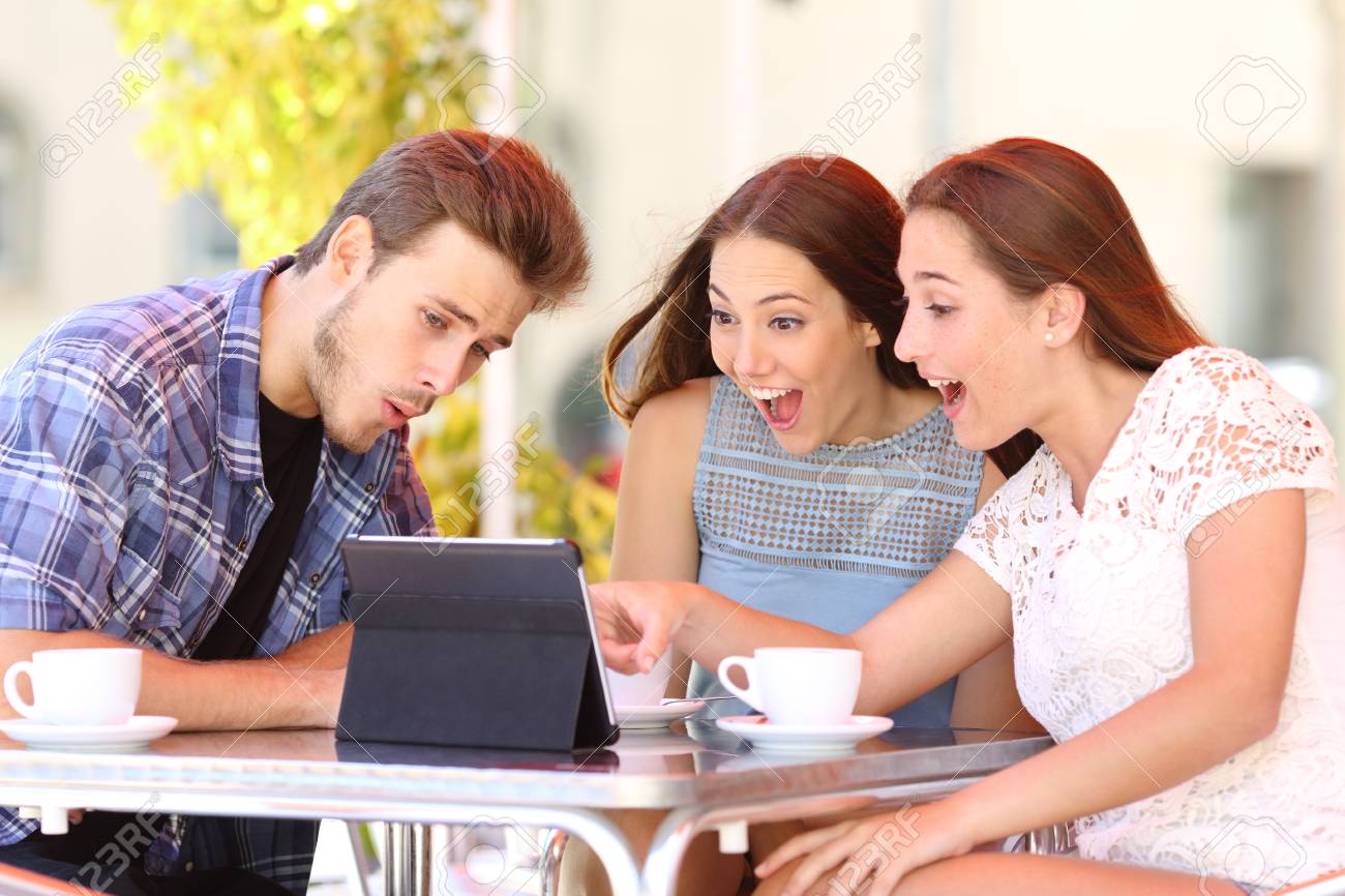 Three excited friends watching tablet content sitting in a coffee shop - 114073577 Three excited friends watching tablet content sitting in a coffee shop - 114073577