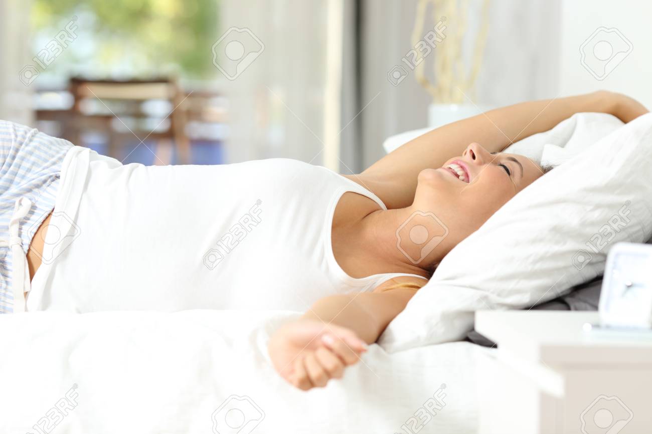Happy woman stretching arms waking up on the bed at home - 115350517 Happy woman stretching arms waking up on the bed at home - 115350517
