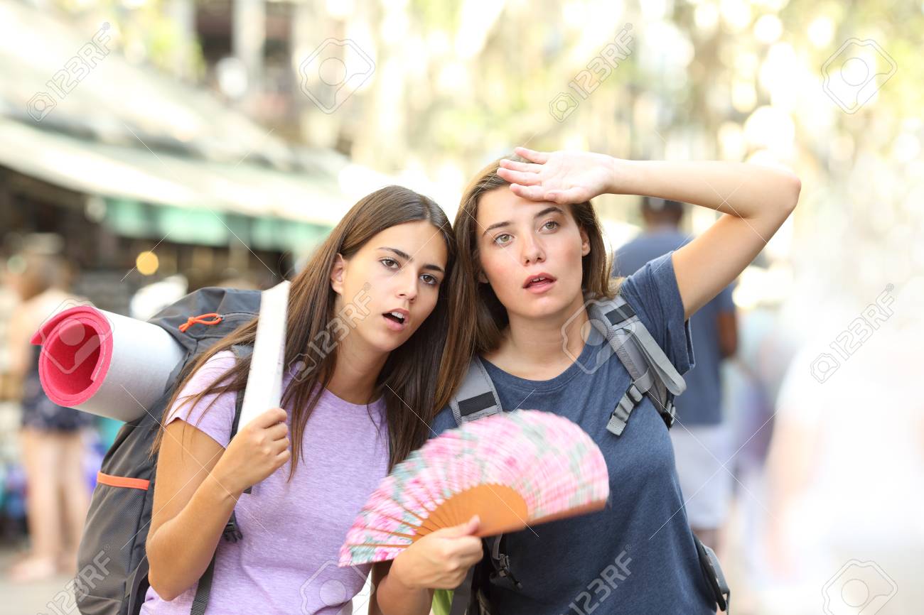 Two backpackers suffering heat stroke walking on the street and fanning on summer vacation - 116123646 Two backpackers suffering heat stroke walking on the street and fanning on summer vacation - 116123646