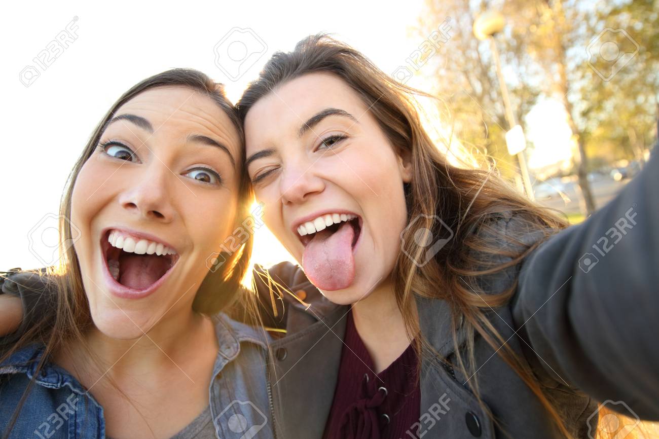 Two funny women joking taking selfies looking at camera in the street - 117941999 Two funny women joking taking selfies looking at camera in the street - 117941999