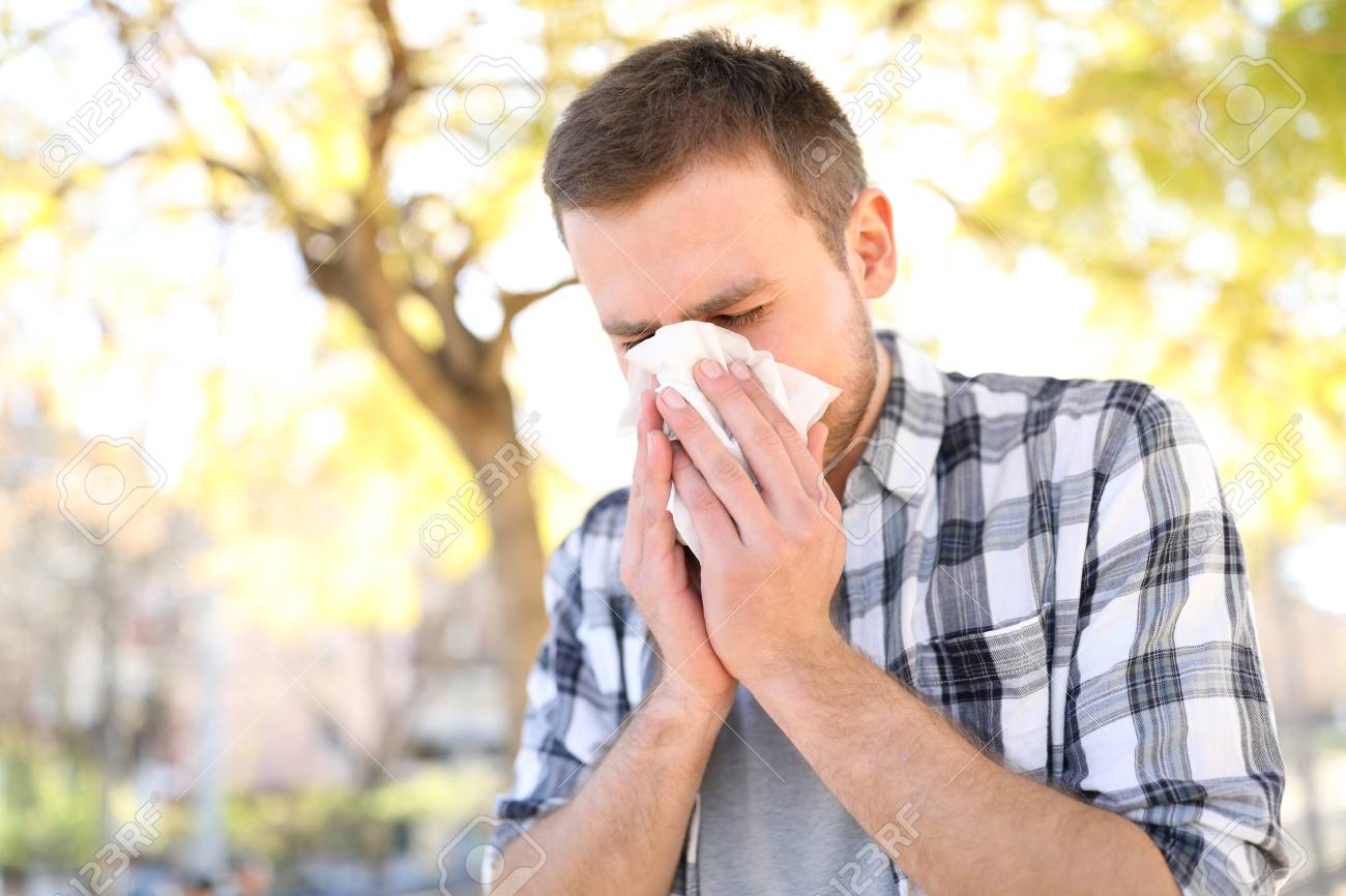 Allergic man sneezing covering nose with wipe in a park in spring season - 117941963 Allergic man sneezing covering nose with wipe in a park in spring season - 117941963
