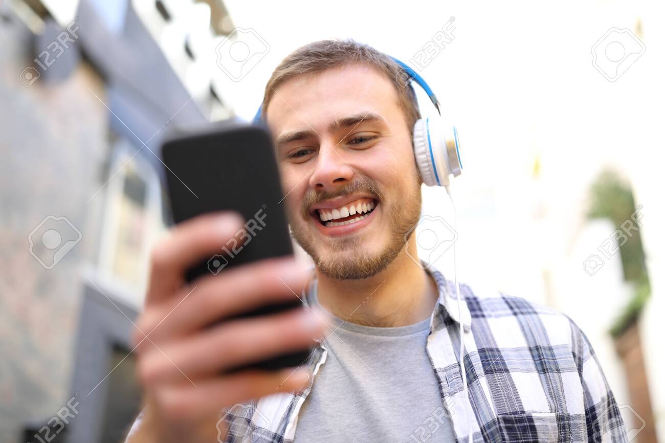 Portrait of a happy man listening to the music with smart phone walking in the street - 128723087 Portrait of a happy man listening to the music with smart phone walking in the street - 128723087