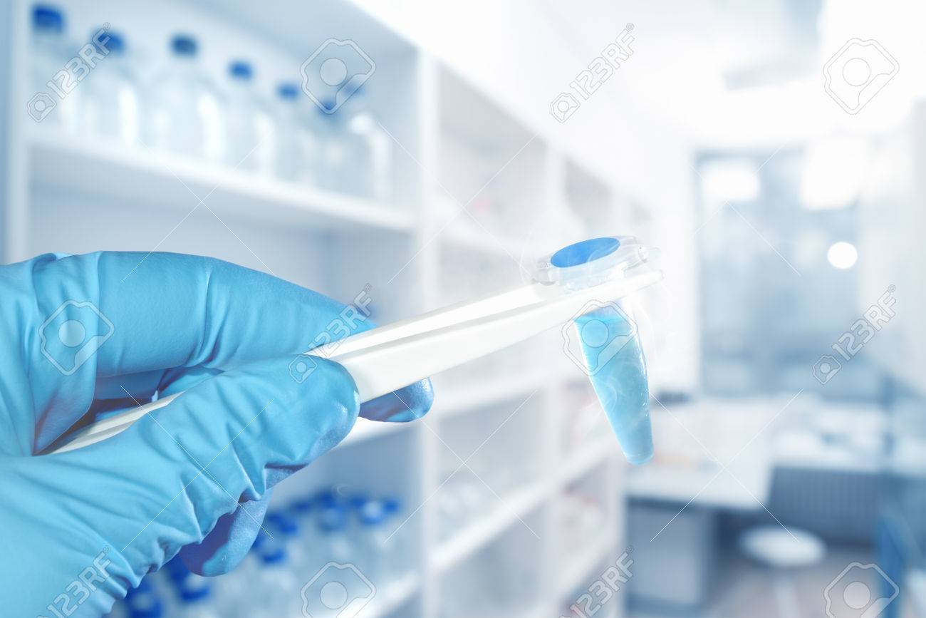 Hand in protective glove holds blue liquid sample, blurred laboratory on the background, focus on the hand, text space - 66725148 Hand in protective glove holds blue liquid sample, blurred laboratory on the background, focus on the hand, text space - 66725148