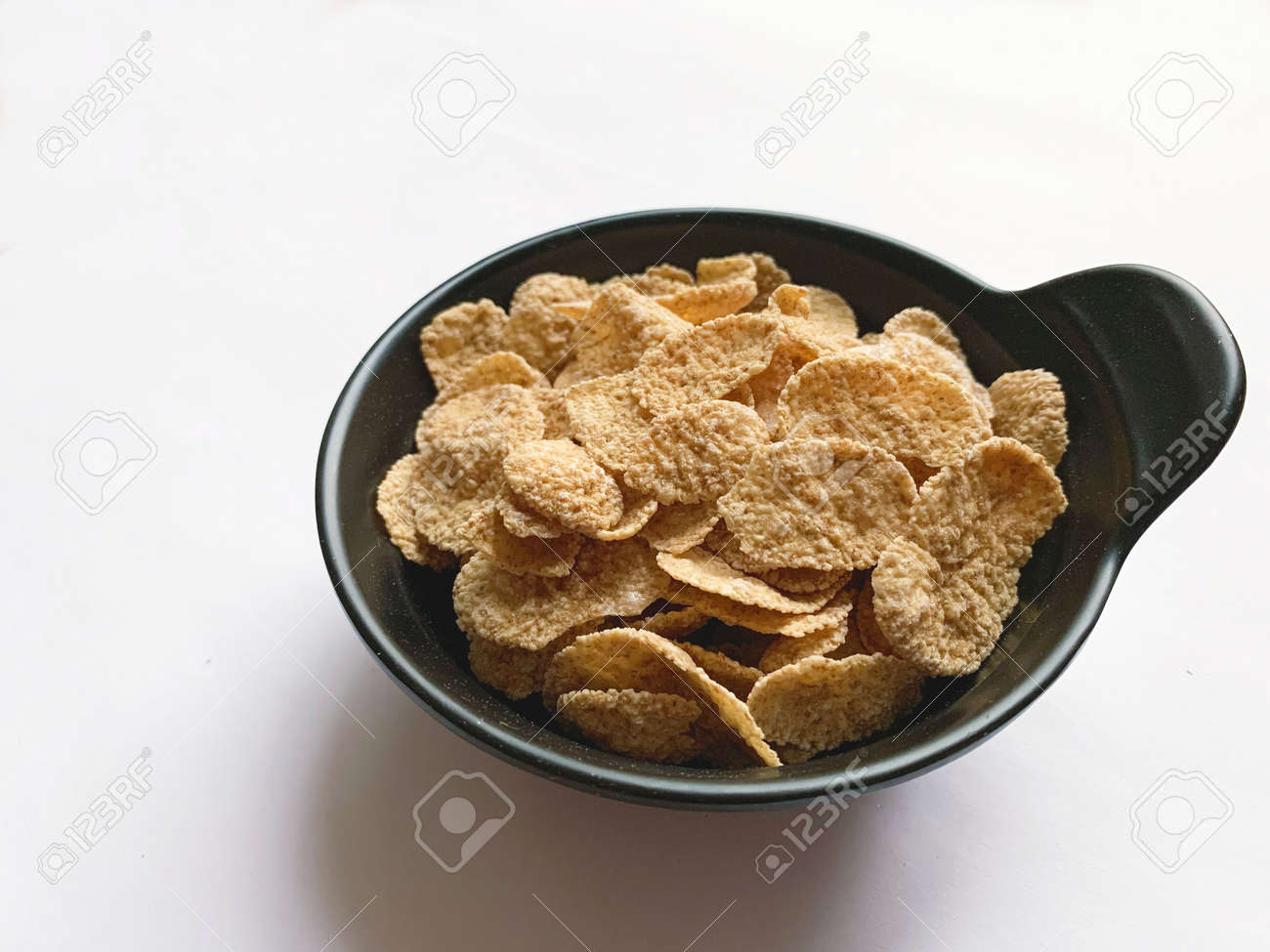 Multi-cereal flakes in a black cup on white background. Closeup. - 169603124 Multi-cereal flakes in a black cup on white background. Closeup. - 169603124